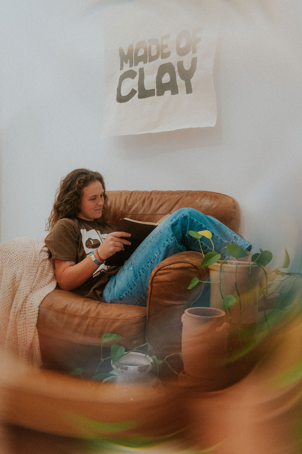 Gabby Gonzales-Heck reading a book in a leather chair, surrounded by clay vessels and plants